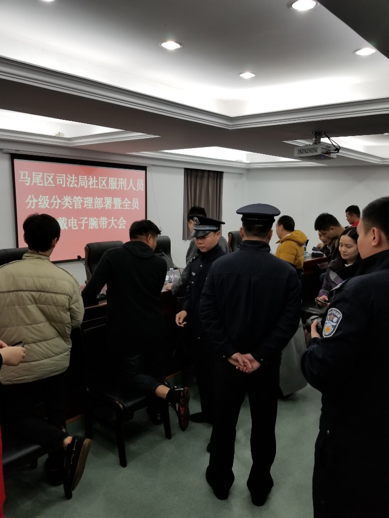 Community corrections staff and law enforcement officers installing electronic monitoring wristbands at Mawei District tiered classification deployment ceremony